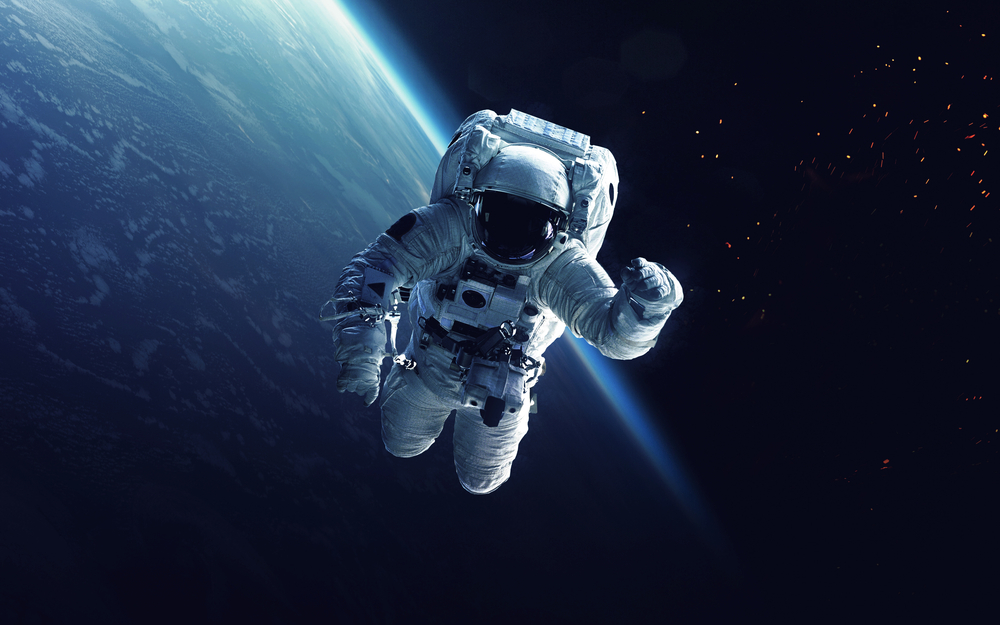 Photograph of an astronaut in space, a blue planet is visible in the background.